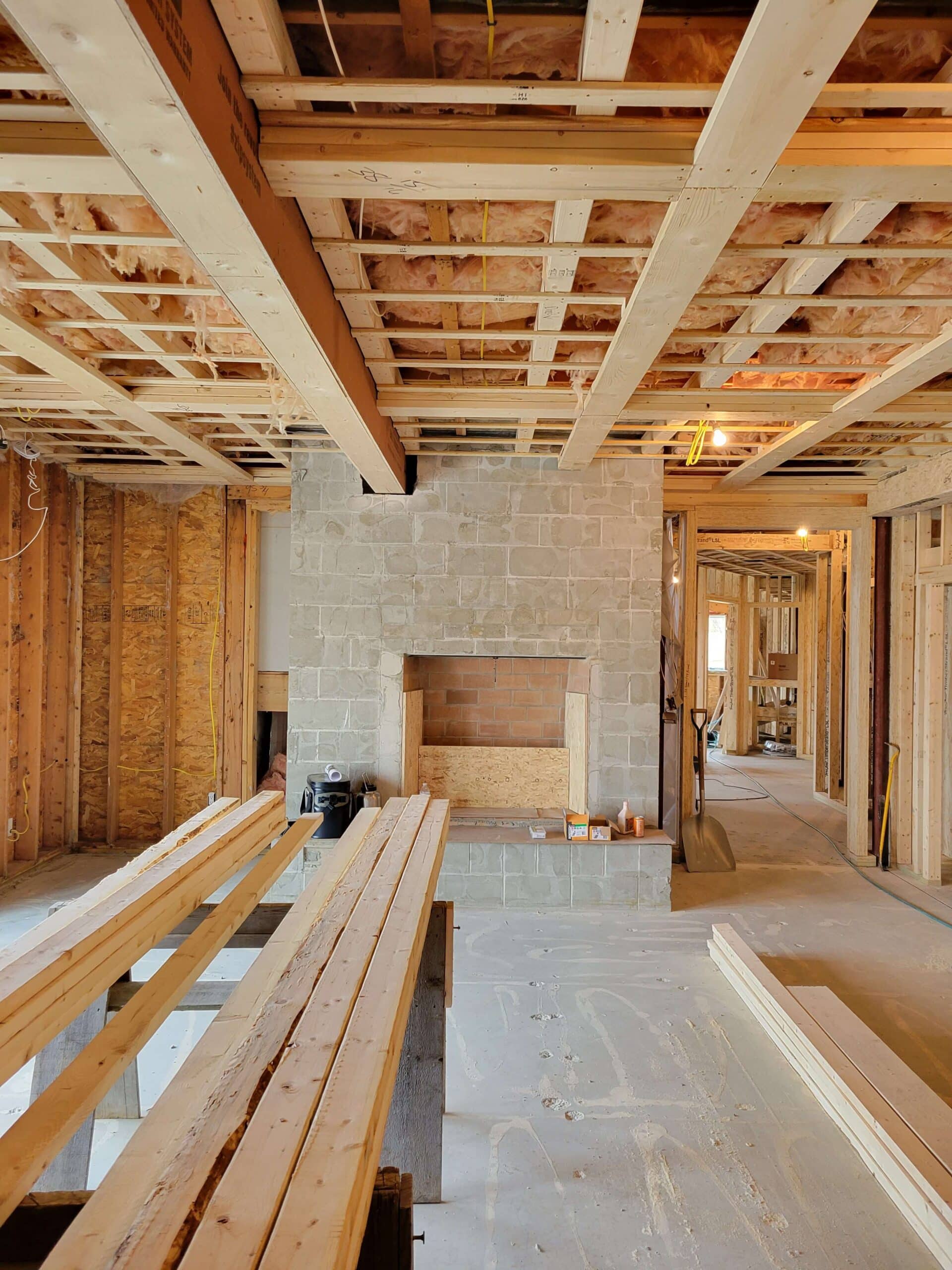 Interior view of a room under construction featuring an exposed wood beam ceiling with insulation and a stone fireplace