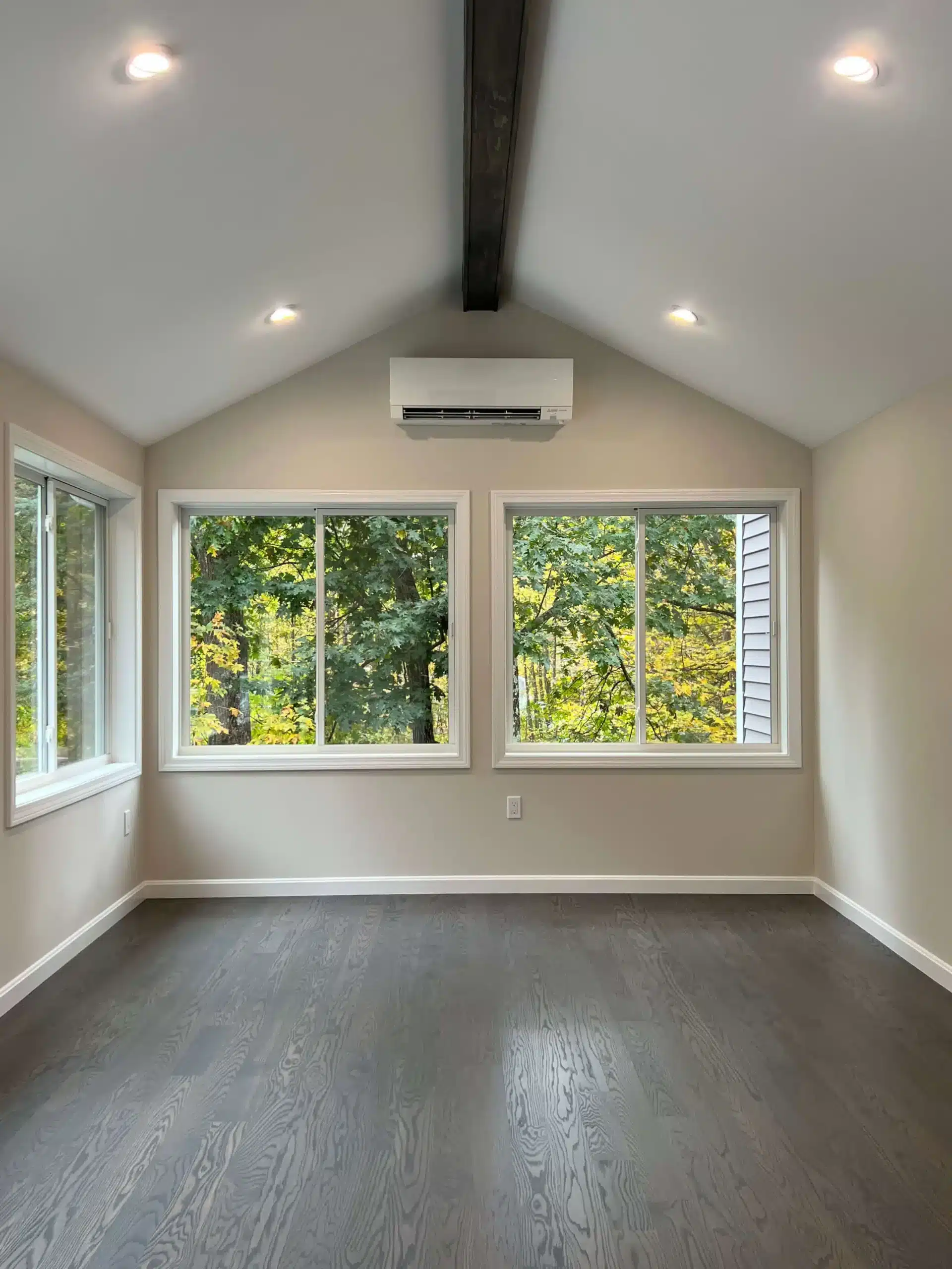 Interior of a newly finished room with a high, vaulted ceiling featuring exposed dark wooden beams and recessed lighting