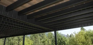 View from below showing the underside of a deck with black metal beams and brown composite decking boards, supported by vertical posts.